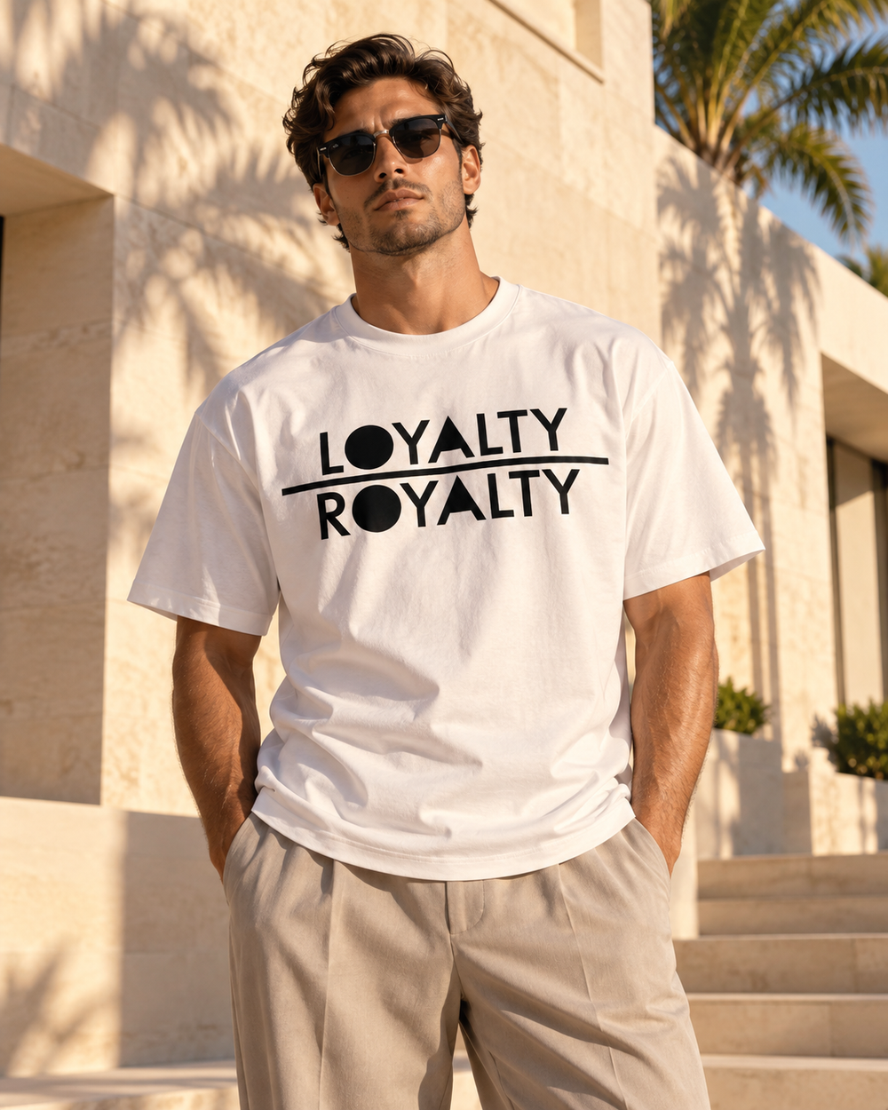 White Loyalty Over Royalty shirt styled with neutral trousers and a palm-lined backdrop